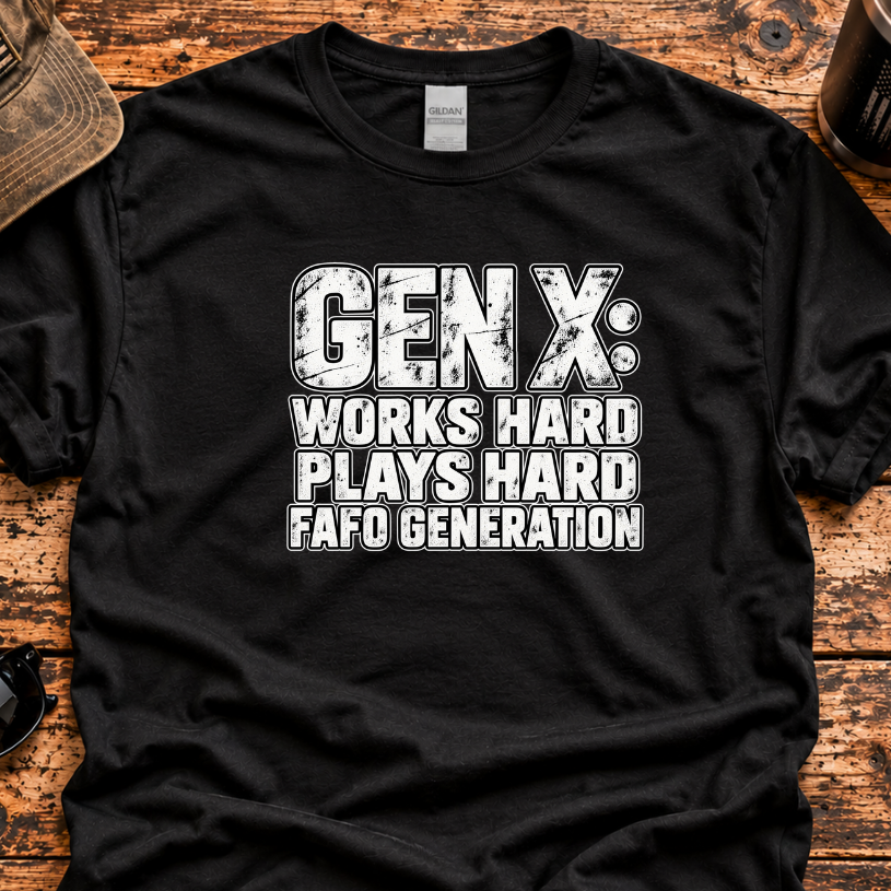 A black short-sleeve graphic T-shirt laid flat on a rustic wooden surface, surrounded by lifestyle props including a distressed cap, sunglasses, a coffee mug, and a knife. The shirt features a bold white distressed text graphic reading 'GEN X: WORKS HARD PLAYS HARD FAFO GENERATION'.