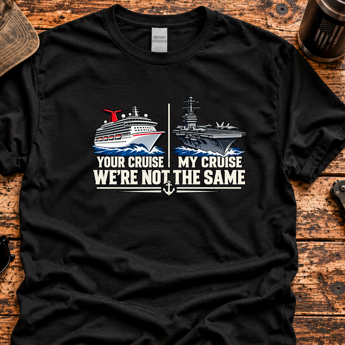 A black short-sleeve graphic T-shirt laid flat on a rustic wooden surface, with a printed design showing a cruise ship on the left and an aircraft carrier on the right, plus the text 'YOUR CRUISE MY CRUISE WE'RE NOT THE SAME.' A cap, sunglasses, coffee mug.